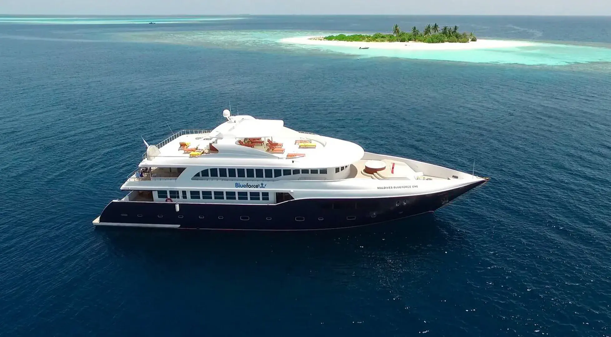 Blue Force One luxury liveaboard moored on a calm lagoon with sundecks and jacuzzis visible.