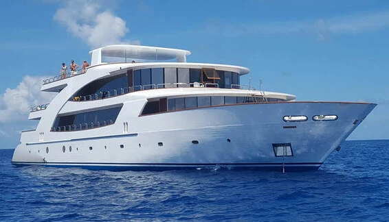Carpe Novo motor yacht cruising over clear blue water with dive dhoni following behind.